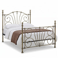 An ornate metal bed frame with a distressed bronze finish, styled with white bedding and a brown throw blanket on a solid white background.