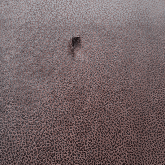 Close-up of a textured brown leather surface with a small hole.
