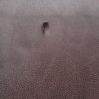 Close-up of a textured brown leather surface with a small hole.