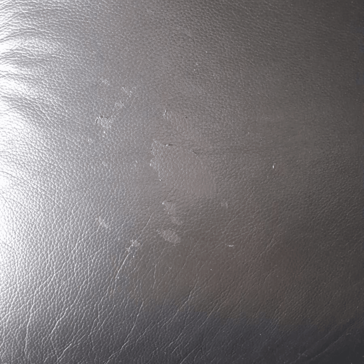 A close-up of a dark gray textured material, resembling leather or faux leather, with visible scuffs and scratches.